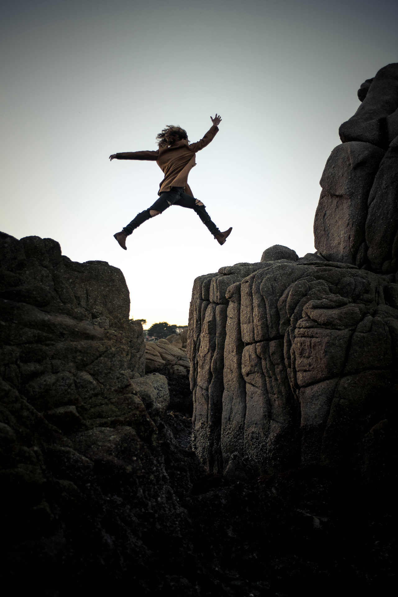 A person leaping between two rocky outcrops at dusk.